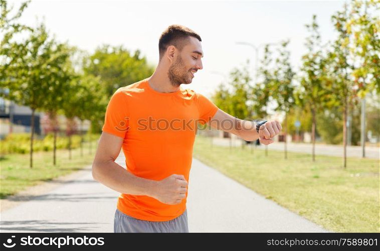 sport, technology and people concept - smiling young man with smart watch or fitness tracker running along road on city street background. smiling man with smart watch running outdoors