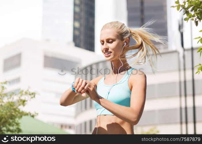 sport, technology and people concept - smiling young woman with fitness tracker and earphones exercising over city street on background. happy woman with fitness tracker and earphones