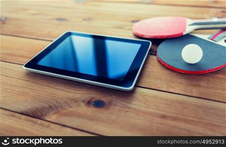 sport, technology, game and objects concept - close up of ping-pong or table tennis rackets with ball and tablet pc computer on wooden floor. close up of table tennis rackets and tablet pc