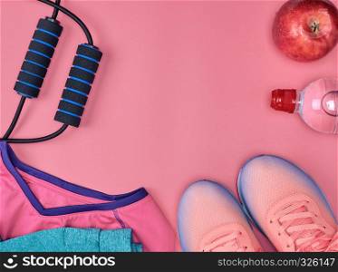 sport textile shoes and other items for fitness on a pink background, top view, copy space