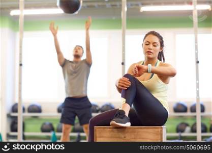 sport, training and people concept - man exercising with medicine ball and woman tracking time on fitness tracker in gym. man and woman with ball and fitness tracker in gym