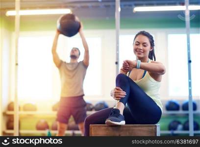 sport, training and people concept - man exercising with medicine ball and woman tracking time on fitness tracker in gym. man and woman with ball and fitness tracker in gym