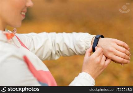sport, training and technology concept - close up of smiling young woman with fitness tracker outdoors in autumn. woman with fitness tracker outdoors in autumn