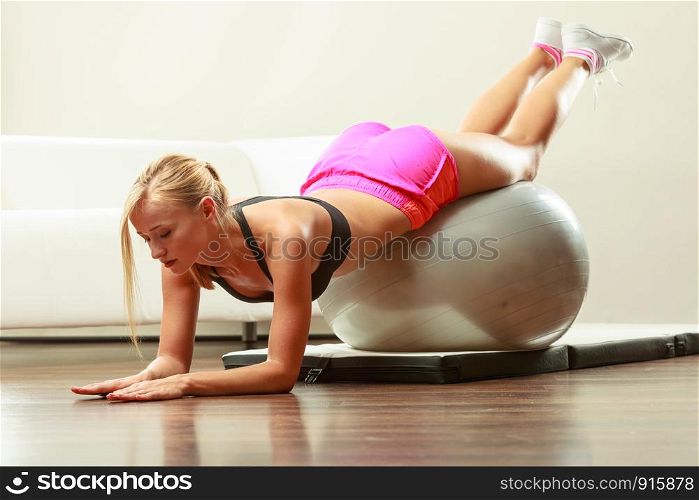 Sport, training, gym and lifestyle concept. Young attractive slim woman in sportswear doing fitness exercises with fit ball at home