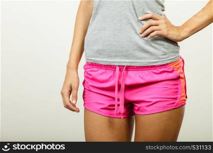 Sport, training, gym and lifestyle concept. Young slim woman in sportswear blue tshirt pink shorts, part of body, female hips.. Female hips in sporty shorts