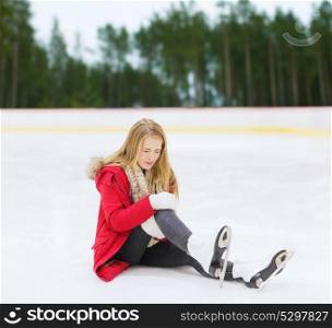 sport, trauma and winter concept - young woman with knee injury suffering from pain on skating rink. young woman with knee injury on skating rink