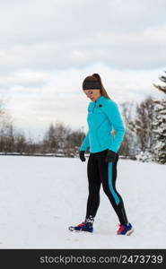 Sport winter people concept. Young lady doing workout in park. Beautiful girl jogging around outside, enjoying wintry time. Woman wearing blue top and leggins.. Young lady doing workout in park.