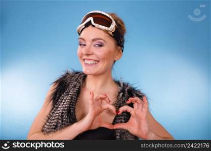 Sport, winter, recreation concept. Young woman with goggle. Lady wearing fur and warm vest making heart shape by hands. Young woman with goggle.