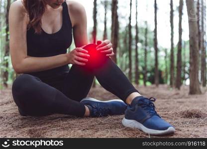 Sport woman injury at knee during jogging in forest. Pine woods background. Medical and Healthcare concept. Nature and People theme. Lifestyles theme. Red light spot use