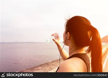Sport woman standing on the bay and drinking water after running