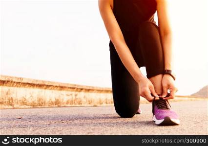 sport woman tying shoelace while running, sunset on the long road