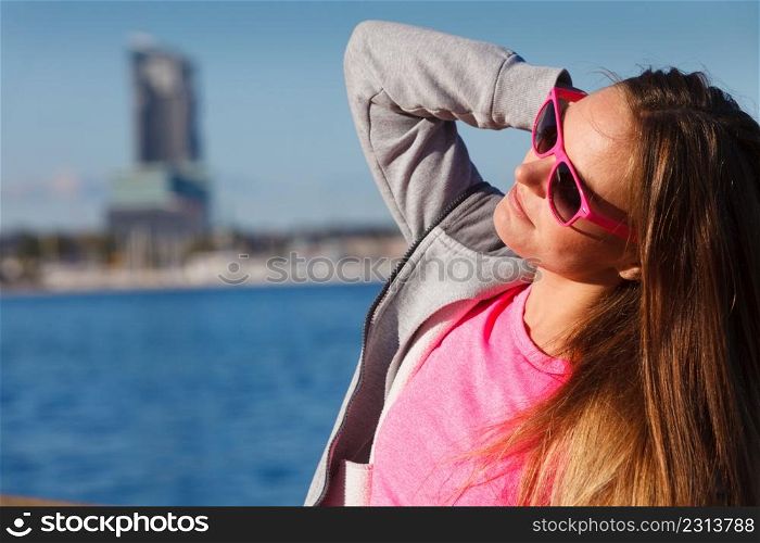 Sport, workout fashion concept. Woman wearing sunglasses and tracksuit resting, relaxing after doing sports outdoors near sea. Woman resting relaxing after doing sports outdoors
