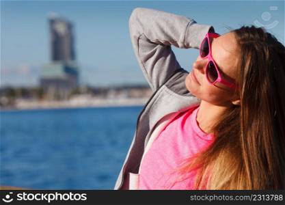 Sport, workout fashion concept. Woman wearing sunglasses and tracksuit resting, relaxing after doing sports outdoors near sea. Woman resting relaxing after doing sports outdoors