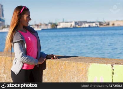 Sport, workout fashion concept. Woman wearing tracksuit resting and relaxing after doing sports outdoors near sea. Woman resting relaxing after doing sports outdoors