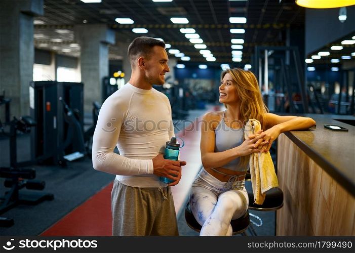 Sportive couple relax at the counter in gym bar after fitness training. Athletic man and woman on workout in sport club, active healthy lifestyle, physical wellness. Sportive couple relax at the counter in gym bar
