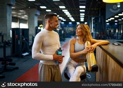 Sportive couple relax at the counter in gym bar after fitness training. Athletic man and woman on workout in sport club, active healthy lifestyle, physical wellness. Sportive couple relax at the counter in gym bar