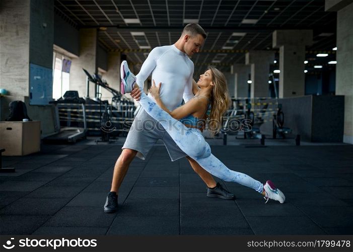 Sportive love couple doing stretching exercise in gym. Athletic man and woman on workout in sport club, active healthy lifestyle, physical wellness. Love couple doing stretching exercise in gym