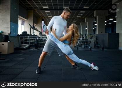 Sportive love couple doing stretching exercise in gym. Athletic man and woman on workout in sport club, active healthy lifestyle, physical wellness. Love couple doing stretching exercise in gym
