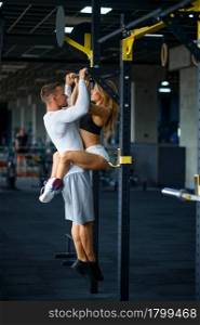 Sportive love couple hugs on horizontal bar, training in gym. Athletic man and woman on workout in sport club, active healthy lifestyle, physical wellness. Sportive love couple hugs on horizontal bar in gym