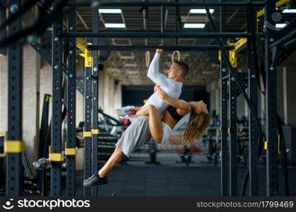 Sportive love couple hugs on horizontal bar, training in gym. Athletic man and woman on workout in sport club, active healthy lifestyle, physical wellness. Sportive love couple hugs on horizontal bar in gym