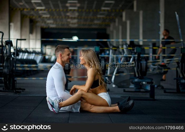 Sportive love couple sitting on the floor, training in gym. Athletic man and woman on workout in sport club, active healthy lifestyle, physical wellness. Love couple sitting on the floor, training in gym