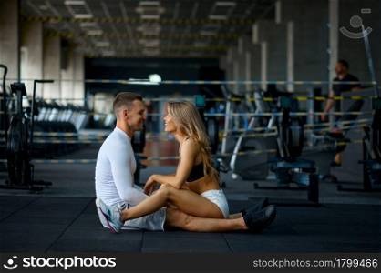 Sportive love couple sitting on the floor, training in gym. Athletic man and woman on workout in sport club, active healthy lifestyle, physical wellness. Love couple sitting on the floor, training in gym