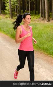 Sportive woman running through forest on summer training day