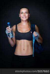 Sportive woman with backpack and bottle of water in hand over dark background, beautiful sportive trainer, active healthy lifestyle