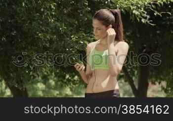 Sports activity, attractive young woman with mp3 player listening to tunes and doing fitness in city park
