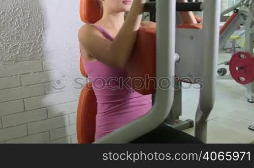 Sports activity young woman working out on weight machine training shoulders and chest in health fitness center jib crane medium shot