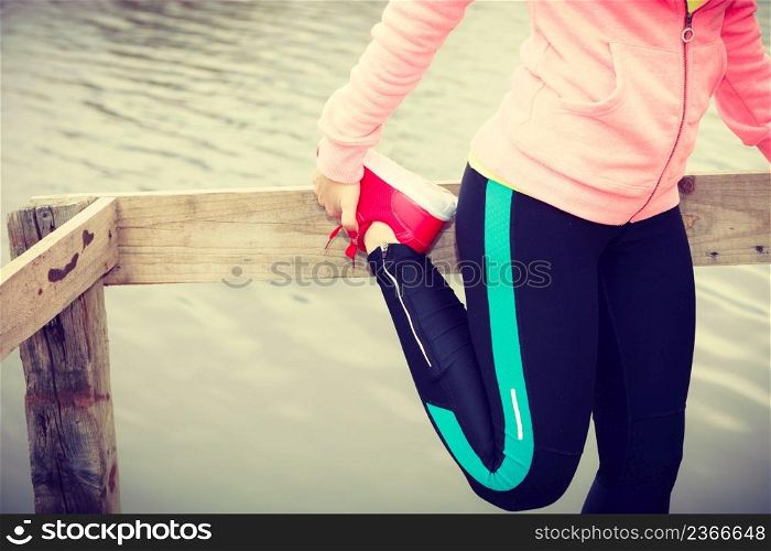 Sports and activities concept. Slim fit attractive woman exercising stretching outdoor. Young motivated girl training in sporty clothes on lake shore. Girl training in sporty clothes on lake shore