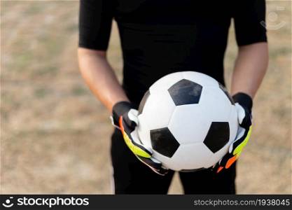 Sports and recreation concept a male teenage goalkeeper wearing black outfit and a pair of colorful gloves holding a soccer.