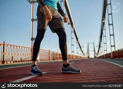 Sports background with male runner feet on bridge road. Closeup sportsman jogger leg in shoe and sportive outfit. Sports background with male runner feet on bridge road