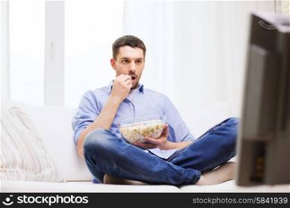 sports, food, happiness and people concept - man watching tv and eating popcorn at home