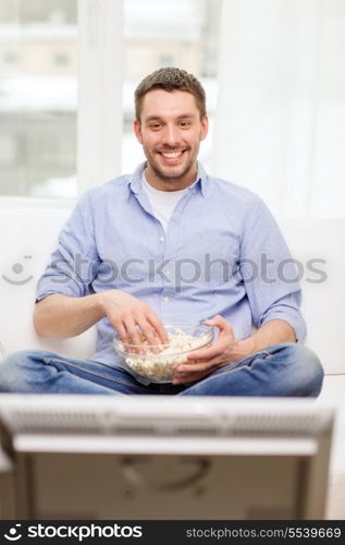 sports, food, happiness and people concept - smiling man with popcorn watching sports on tv and supporting team at home