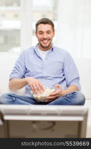 sports, food, happiness and people concept - smiling man with popcorn watching sports on tv and supporting team at home