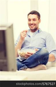 sports, food, happiness and people concept - smiling man with popcorn watching sports on tv and supporting team at home