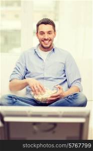sports, food, happiness and people concept - smiling man with popcorn watching sports on tv and supporting team at home
