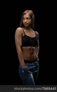 Sports girl 20 years in jeans with bare belly in the studio on a black background.