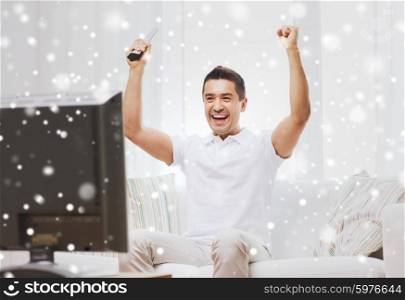 sports, happiness and people concept - smiling man watching sports on tv and supporting team at home over snow effect