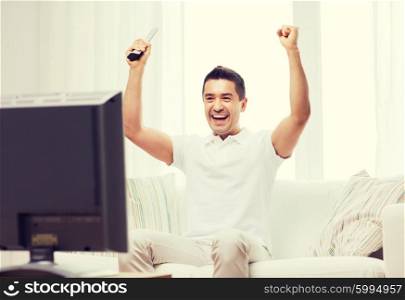 sports, happiness and people concept - smiling man watching sports on tv and supporting team at home