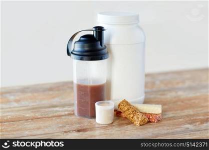 sports nutrition, fitness diet and food concept - jar, protein shake bottle and muesli bars on wooden table. food and sports nutritional additives on table