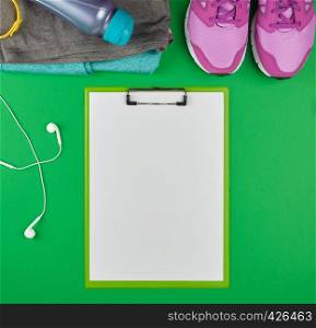 sports women's clothing for sports and fitness, top view, green background, in the middle of the holder for the paper with empty white sheets