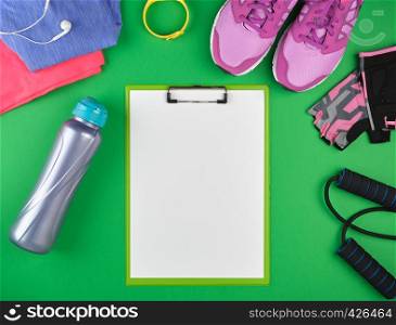 sports women's clothing for sports and fitness, top view, green background, in the middle of the holder for the paper with empty white sheets