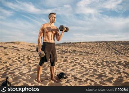 Sportsman doing exercises with weights in desert at sunny day. Strong motivation in sport, strength outdoor training. Sportsman doing exercise with weights in desert