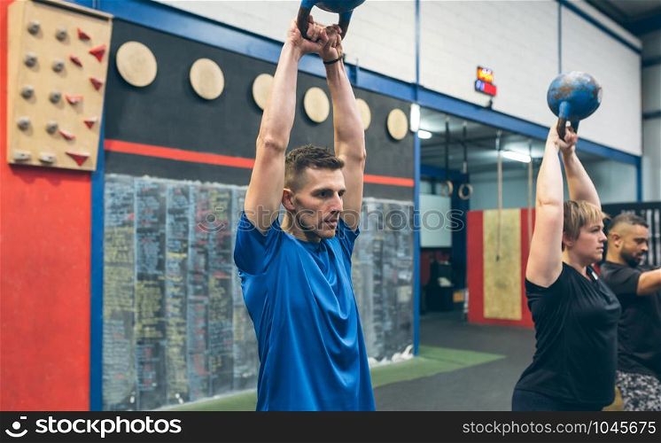 Sportsman exercising with kettlebell with his partners in the gym. Sportsman exercising with kettlebell with his partners