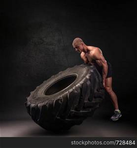 Sportsman lifting large heavy wheel in a gym. Sportsman lifting heavy wheel