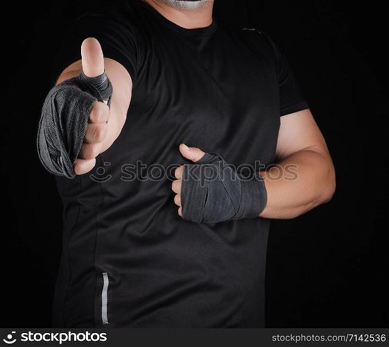 sportsman&rsquo;s hands wrapped in black elastic sports bandage show a like sign, dark background