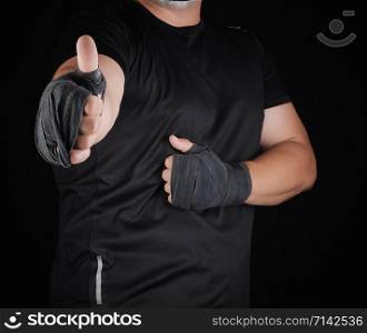 sportsman&rsquo;s hands wrapped in black elastic sports bandage show a like sign, dark background