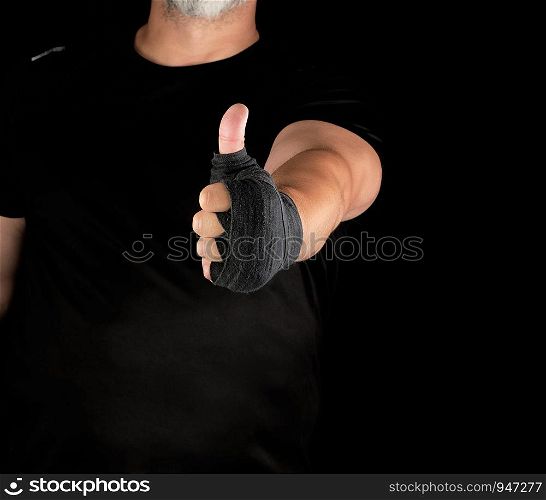 sportsman's hands wrapped in black elastic sports bandage show a like sign, dark background